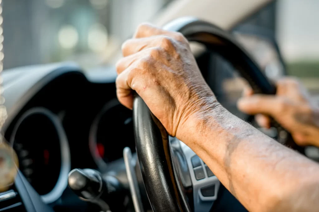 Shutterstock_2476681191 - ByznysDeník Ruce staršího řidiče pevně svírající volant