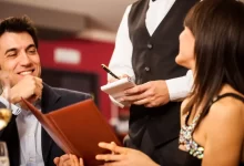 Dva lidé v luxusní restauraci si objednávají jídlo u číšníka.