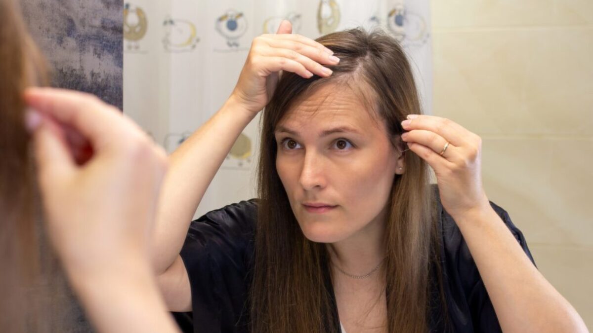 Žena v zrcadle prohlíží své řídnoucí vlasy