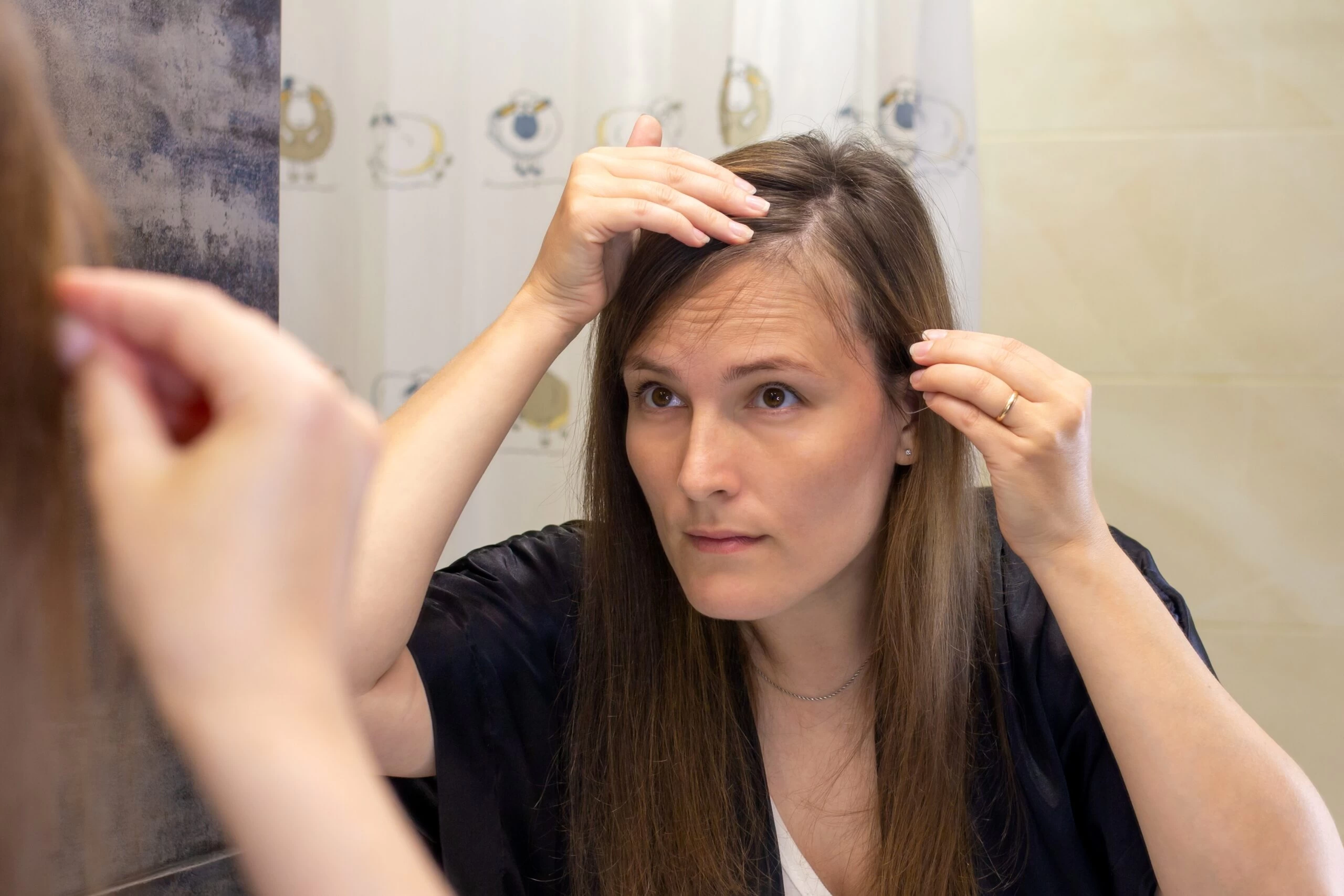 Žena v zrcadle prohlíží své řídnoucí vlasy