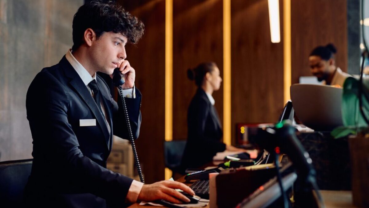 Hotelová recepce, recepční telefonuje a hledí do PC