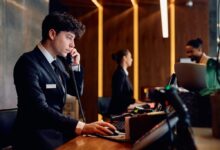 Hotelová recepce, recepční telefonuje a hledí do PC