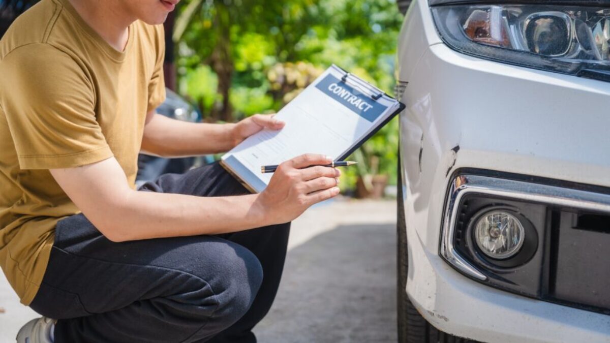 Muž sedí vedle auta a zapisuje dokument - záznam o autonehodě