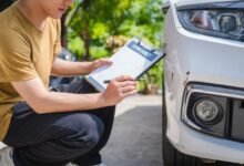 Muž sedí vedle auta a zapisuje dokument - záznam o autonehodě