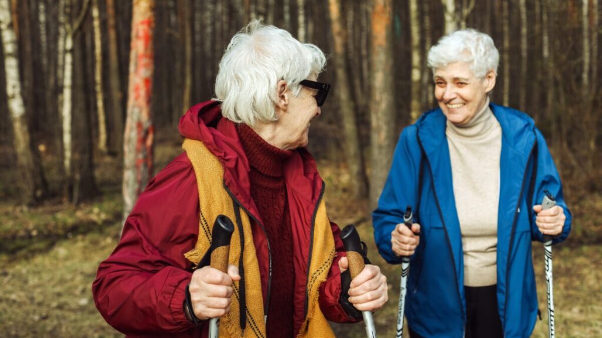 Dvě starší ženy na procházce lesem s holemi nordic walking