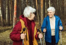 Dvě starší ženy na procházce lesem s holemi nordic walking