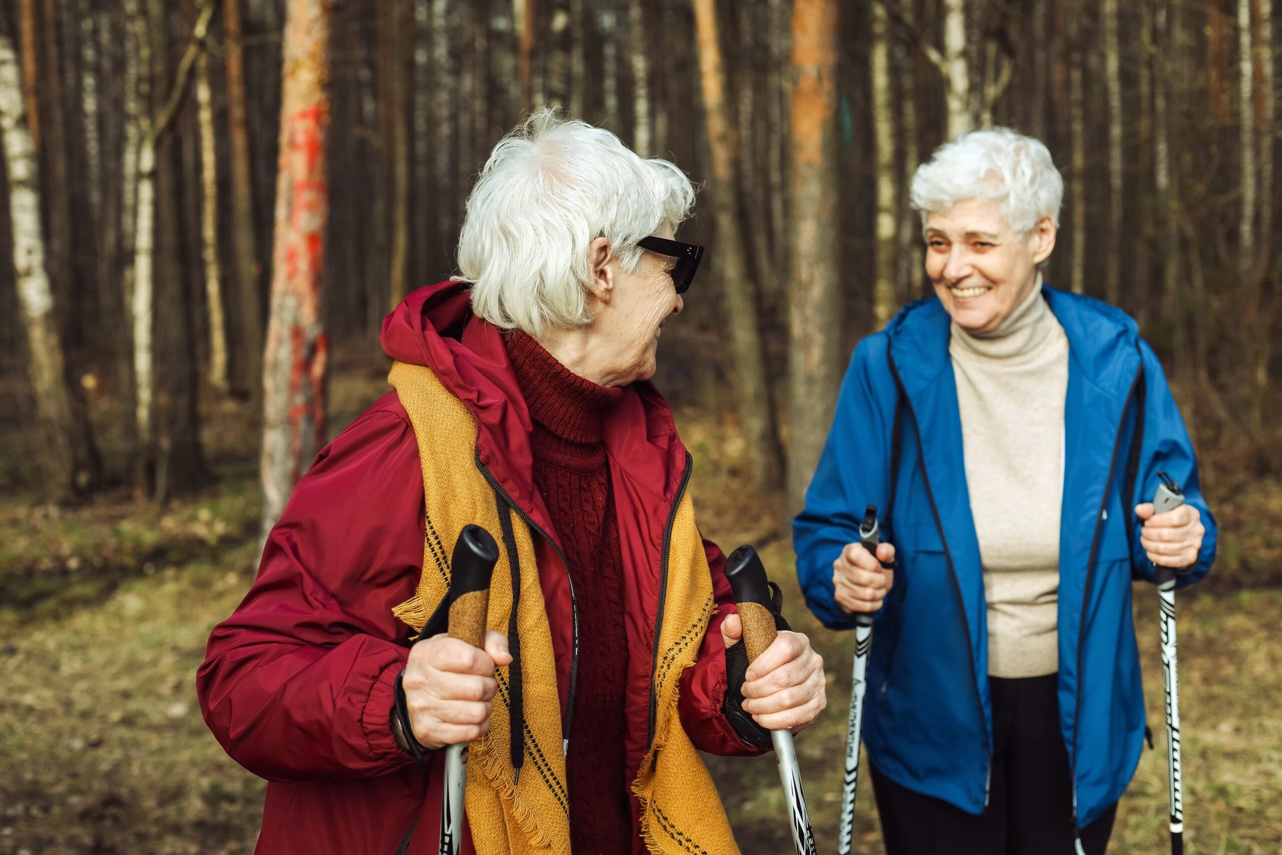 Dvě starší ženy na procházce lesem s holemi nordic walking