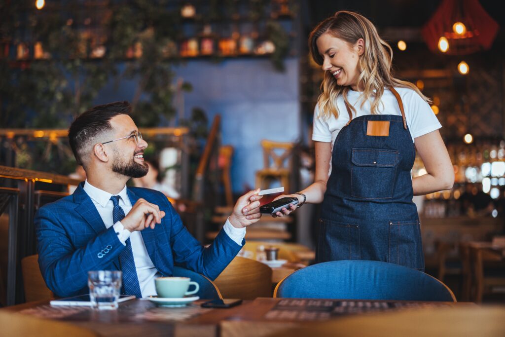 V restauracích by vám měli přinést platební terminál ke stolu. Kartu z ruky nedávejte, Zdroj: Shutterstock.com - ByznysDeník Muž se usmívá na servírku a platí kartou útratu přes terminál