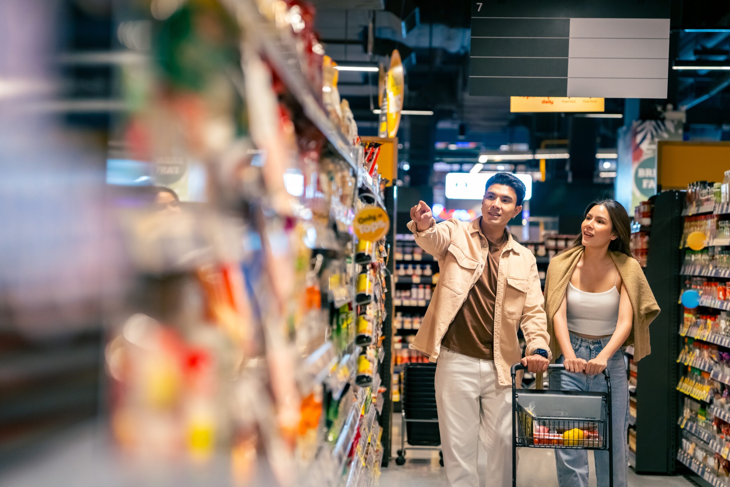 Šťastný asijský pár nakupuje v supermarketu a tlačí košík