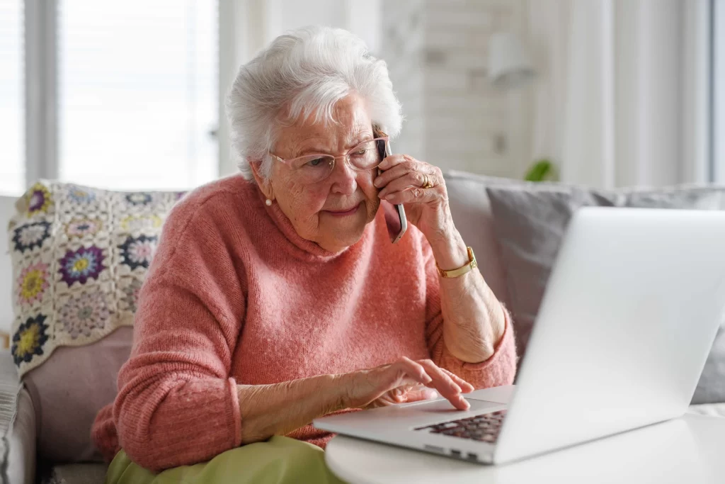 shutterstock_2464275873_optimized - ByznysDeník seniorka telefonu a pracuje na počítači