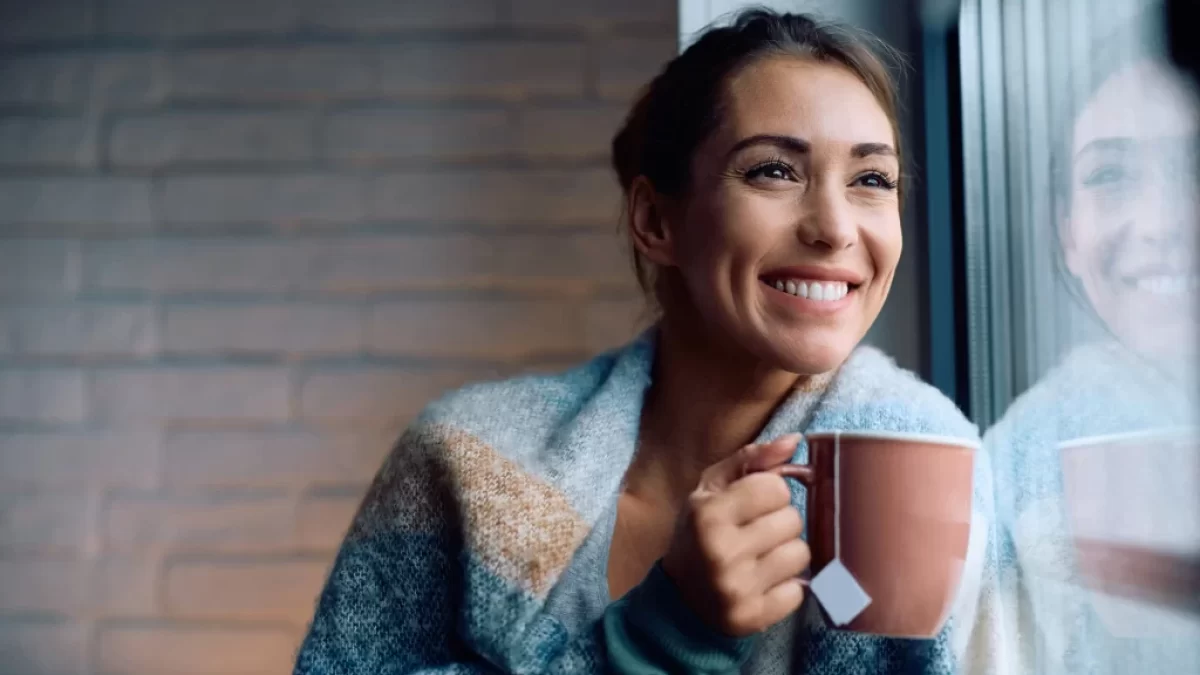 Žena dívající se z okna s hrnkem čaje.