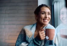 Žena dívající se z okna s hrnkem čaje.