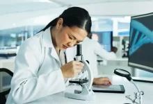 Žena dívající se do mikroskopu, zkoumající DNA.