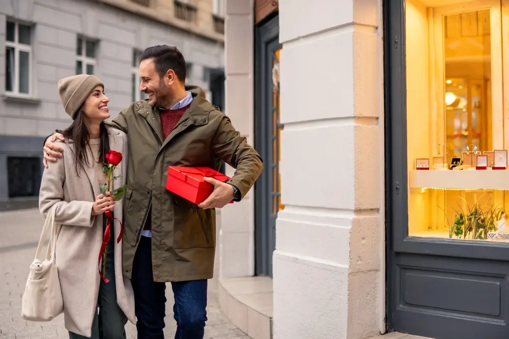 shutterstock_2565536435 - ByznysDeník Muž s dárkem v ruce a žena držící růži se drží za ramena.