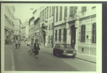 Žena procházející v ulici kolem auta v roce 1980.