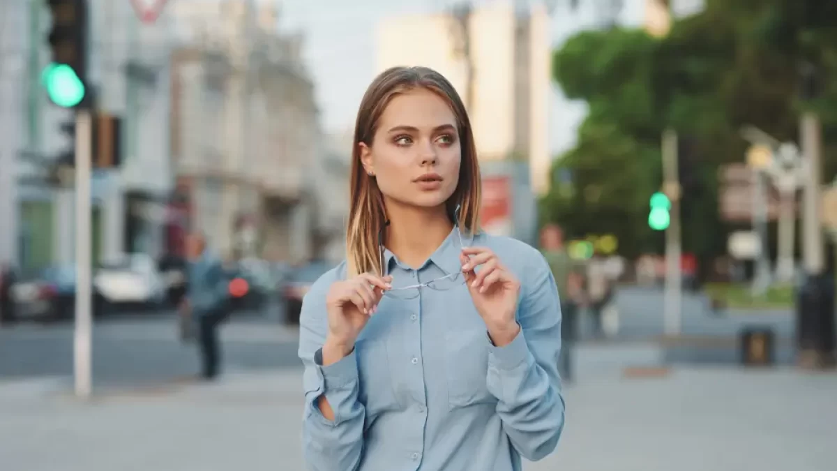 Žena na ulici pózuje s brýlemi.