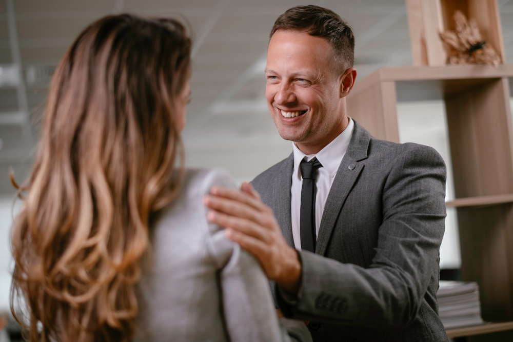 BusinessmanAndBusinesswomanInOfficeYoungWomanAndManFlirting - ByznysDeník Muž sahá kolegyni na rameno.