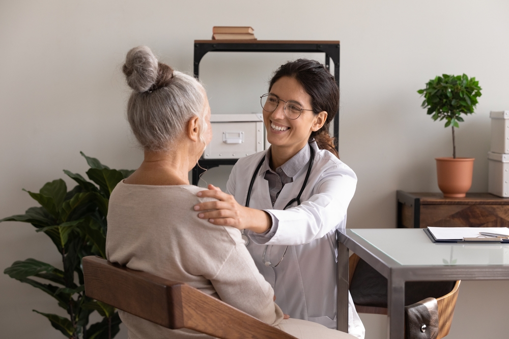 HappySatisfiedGpDoctorTellingGoodNewsToElderPatient - ByznysDeník Lékařka drží za rameno pacientku.