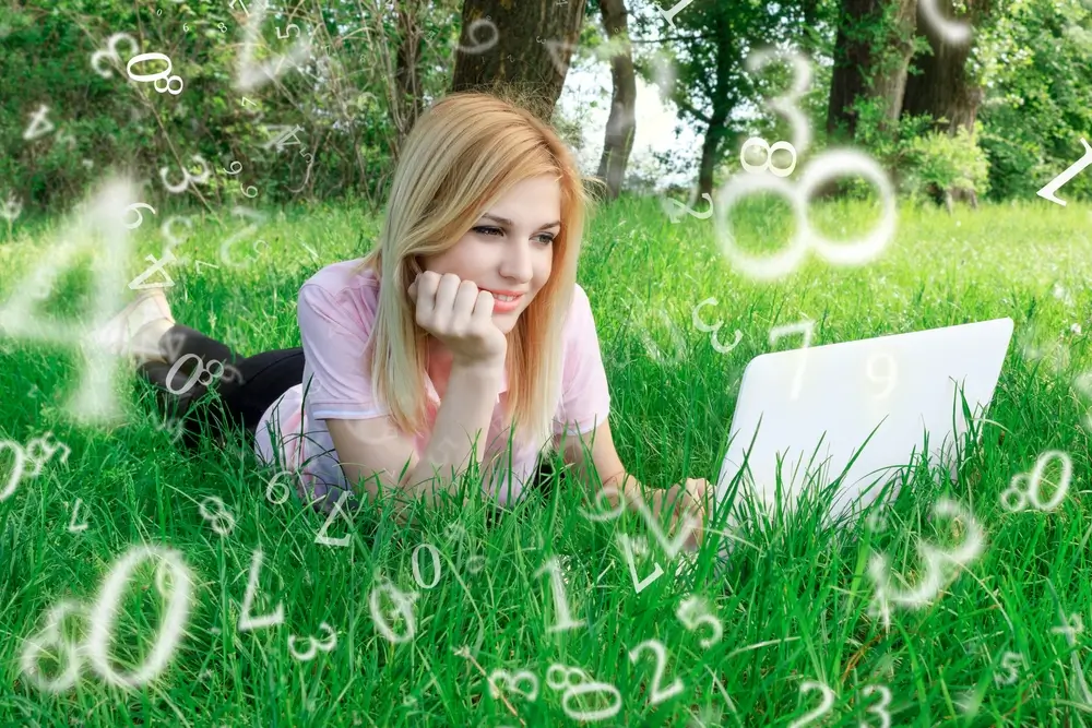 Žena leží v trávě s notebookem. Okolo ní jsou čísla.