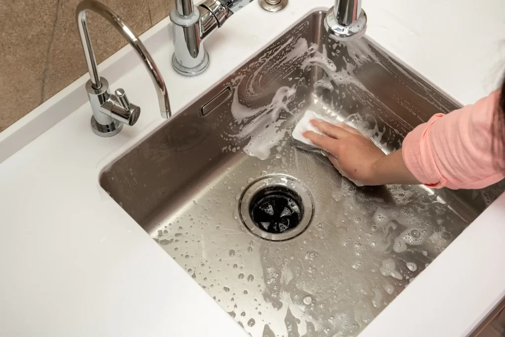Ucpání odpadu se dá předejít. Zdroj: Shutterstock - ByznysDeník Ruka ženy čistící dřez v kuchyni.
