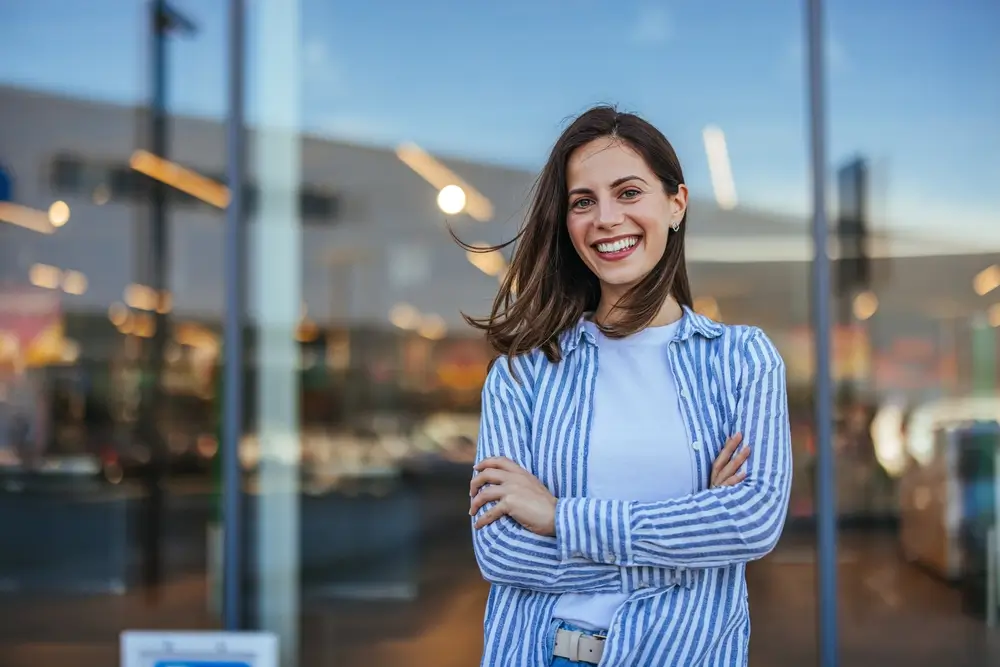 shutterstock_2500022355 - ByznysDeník Žena v košili před moderní budovou se usmívá.