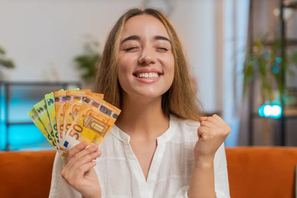 shutterstock_2549967225 1 - ByznysDeník Žena drží v ruce peníze a raduje se.