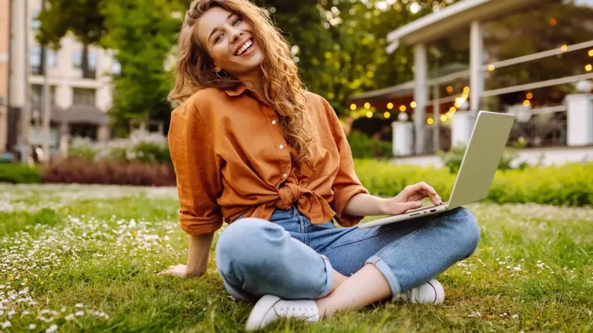 Žena sedí na trávě s notebookem.