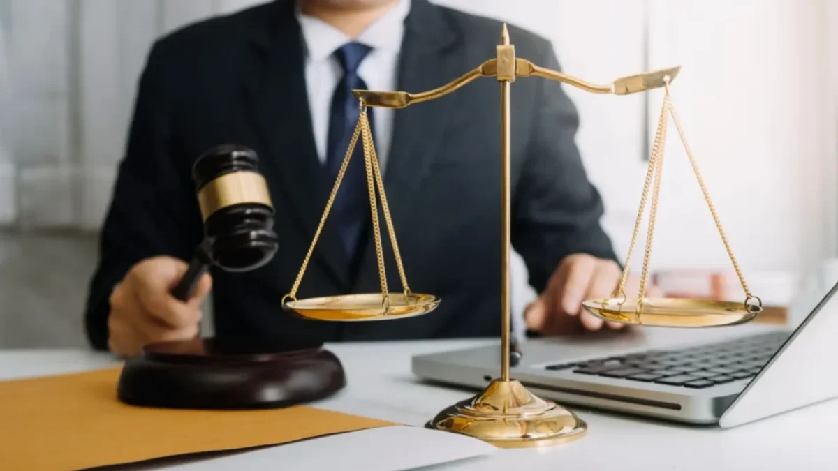 Muž v obleku drží kladívko u stolu vedle zlatých vah a otevřeného notebooku