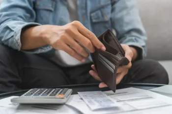 Muž držící prázdnou peněženku u stolu s účty a kalkulačkou