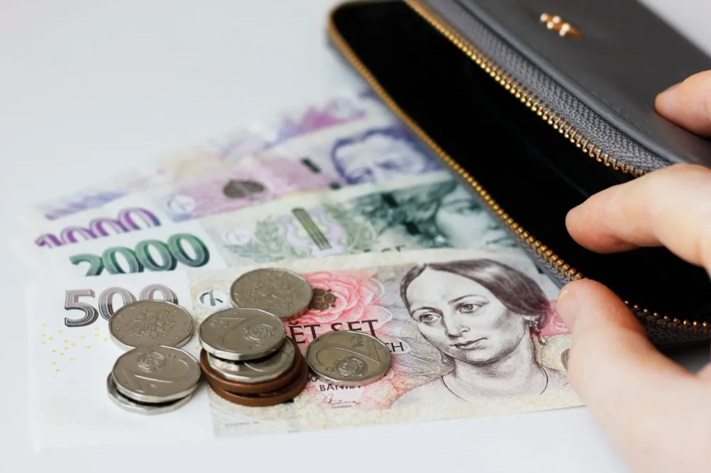 Otevřená peněženka s českými bankovkami v hodnotě 500, 1000 a 2000 korun a drobnými mincemi rozloženými na stole.
