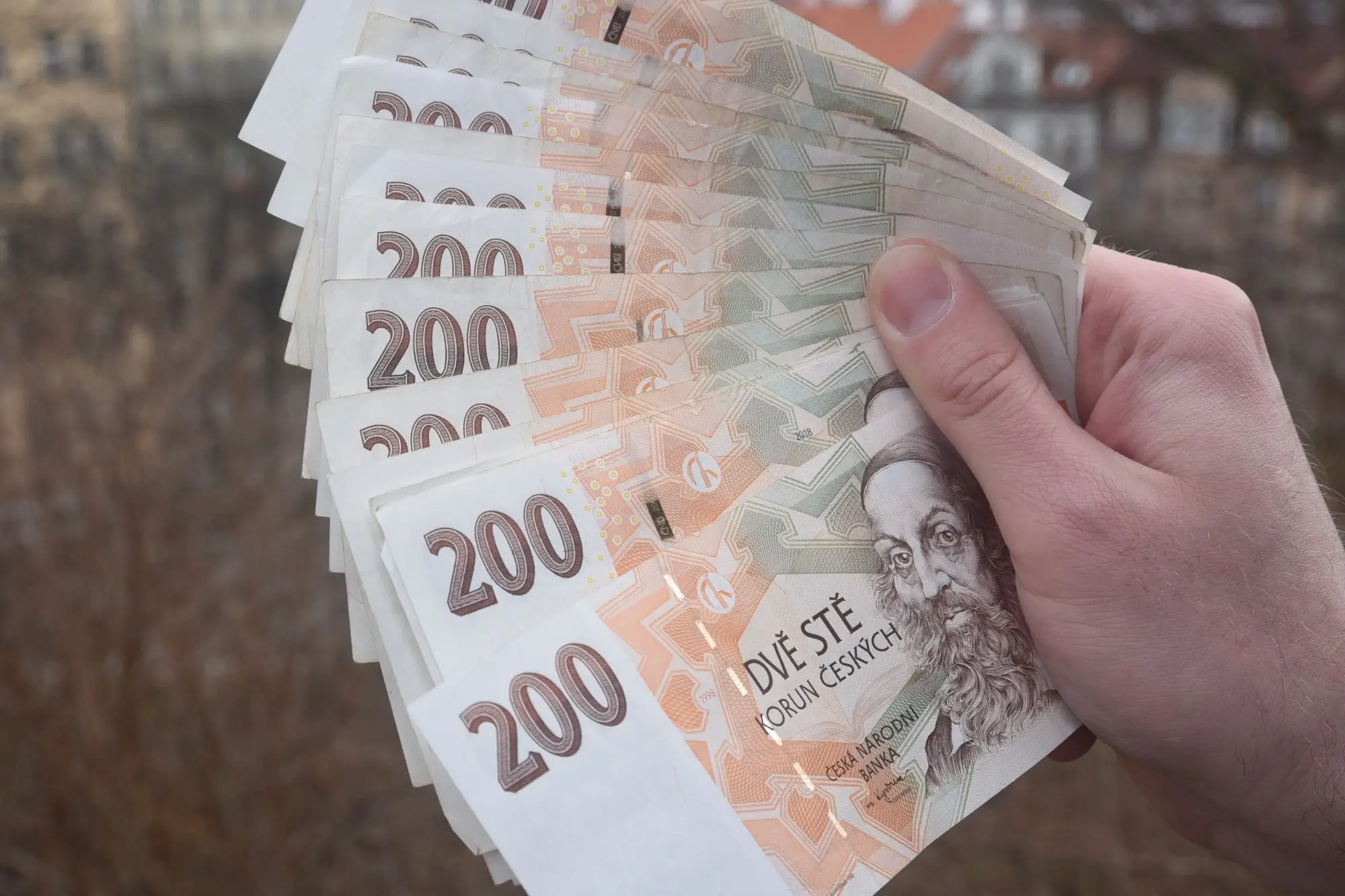 Ruka držící vějíř z několika českých bankovek v hodnotě 200 korun.