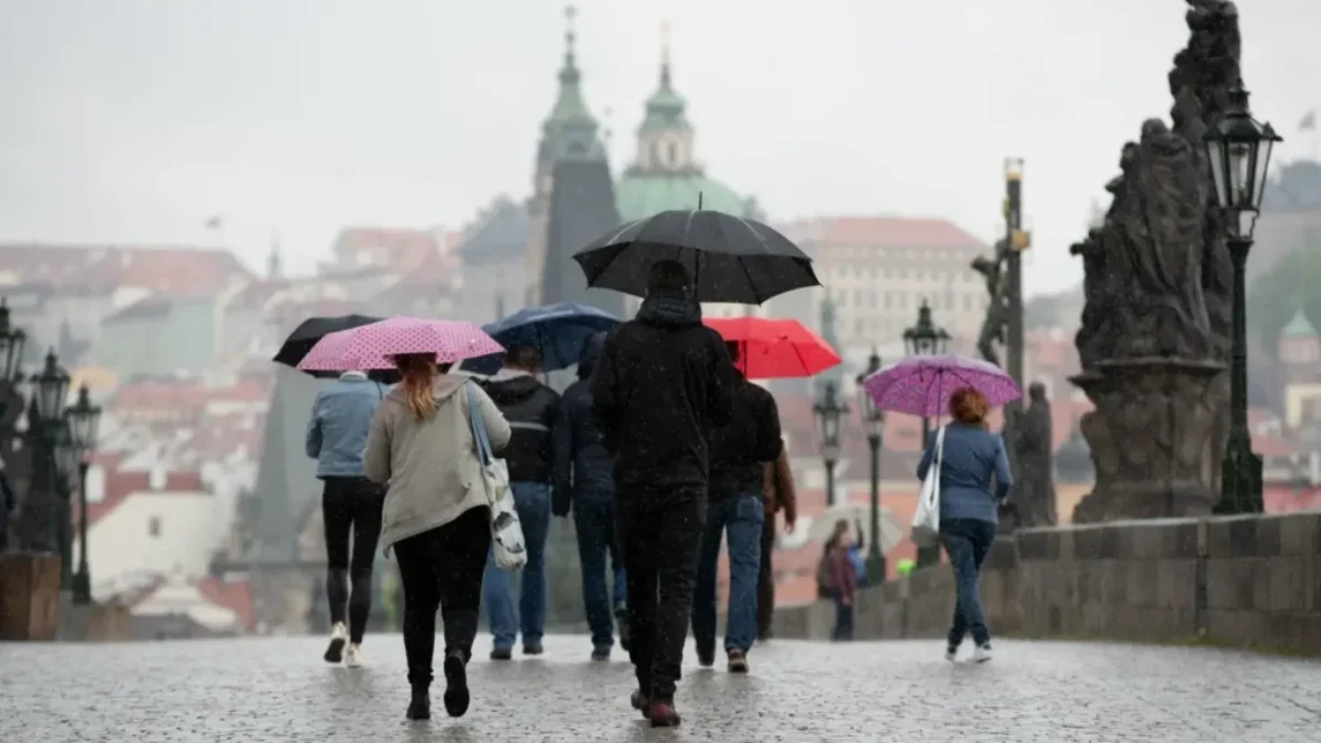 Skupina lidí s barevnými deštníky přechází Karlův most v Praze
