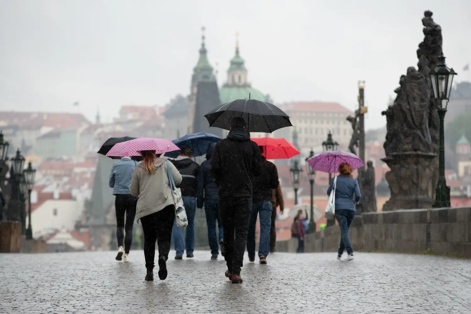 Skupina lidí s barevnými deštníky přechází Karlův most v Praze