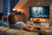 Dvojice sedí na gauči a sleduje akční film prostřednictvím streamovací služby na velké obrazovce