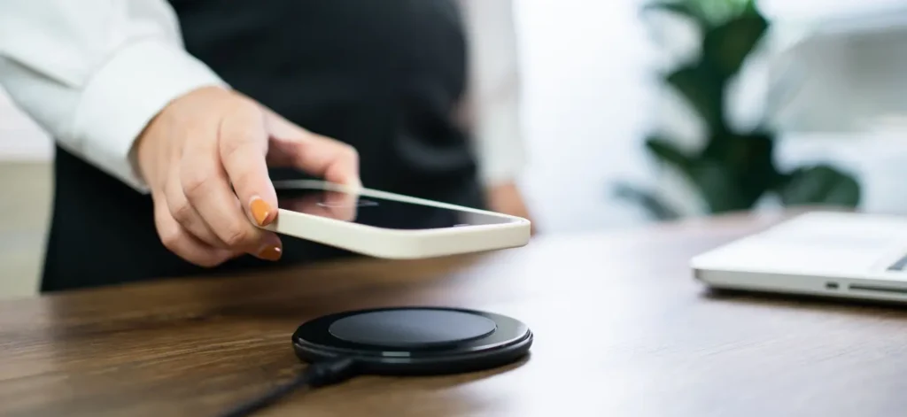 Žena pokládá chytrý telefon na bezdrátovou nabíjecí podložku na pracovním stole