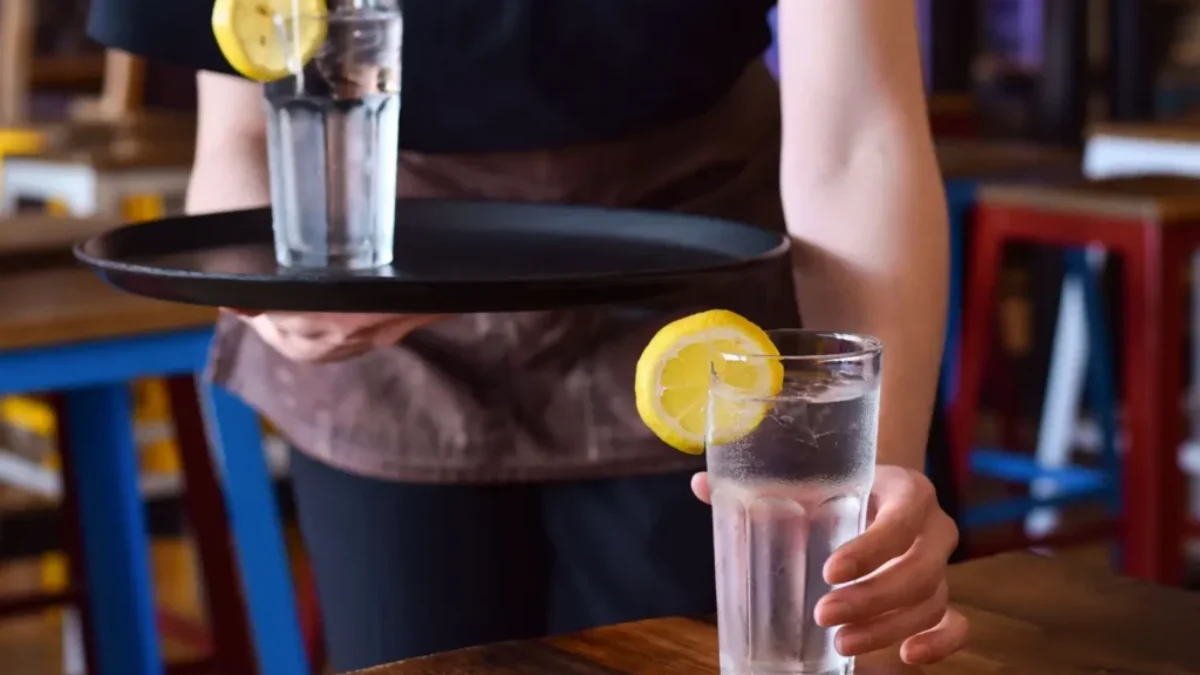 Servírka přináší hostovi sklenici vody s plátkem citronu na podnose v restauraci