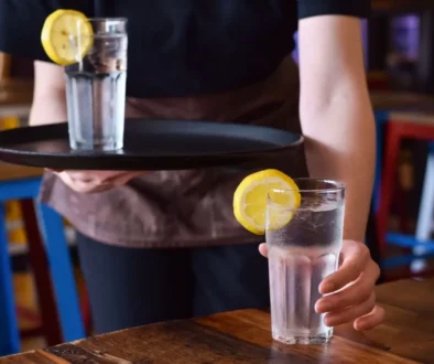 Servírka přináší hostovi sklenici vody s plátkem citronu na podnose v restauraci