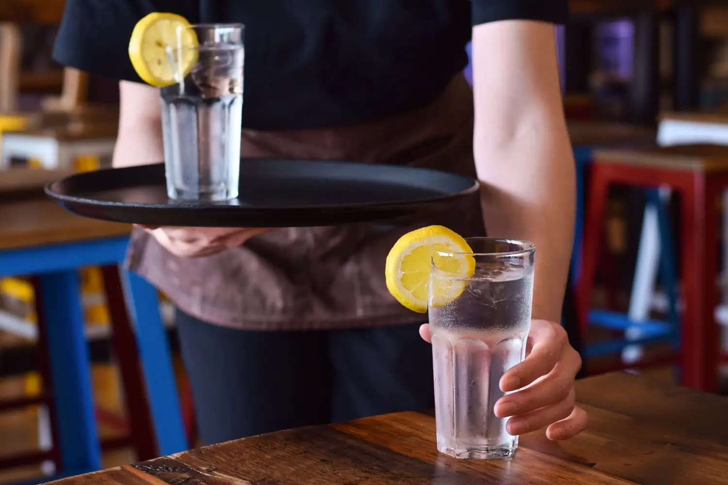 Servírka přináší hostovi sklenici vody s plátkem citronu na podnose v restauraci