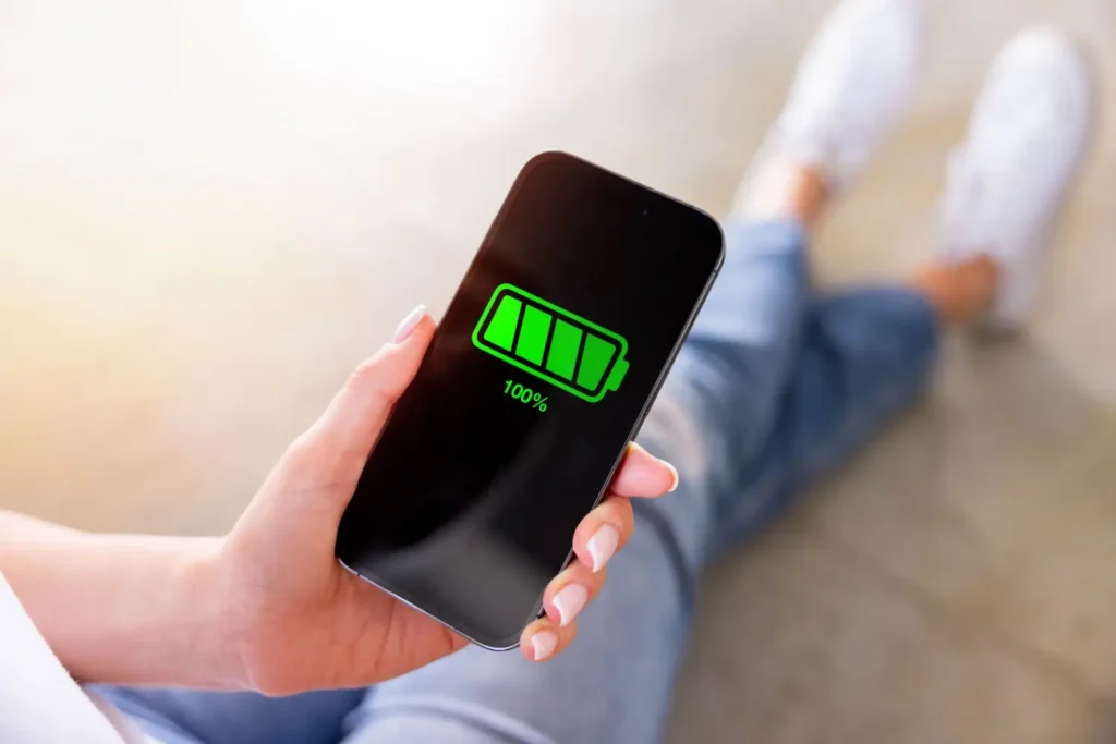 Smartphone v ruce ženy s ikonou stoprocentně nabité baterie na displeji