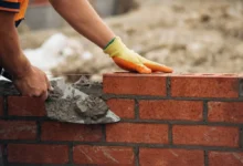 Zedník pečlivě pokládá cihly a uhlazuje maltu při stavbě rovné zdi na staveništi