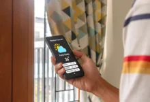 Ruka drží telefon se zobrazenou předpovědí počasí a ikonou slunce