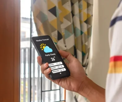 Ruka drží telefon se zobrazenou předpovědí počasí a ikonou slunce