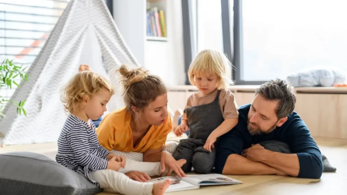 Rodina s malými dětmi společně čte knihu na podlaze obývacího pokoje