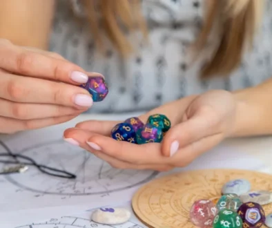 Žena drží astrologické kostky nad horoskopickým kolem na stole