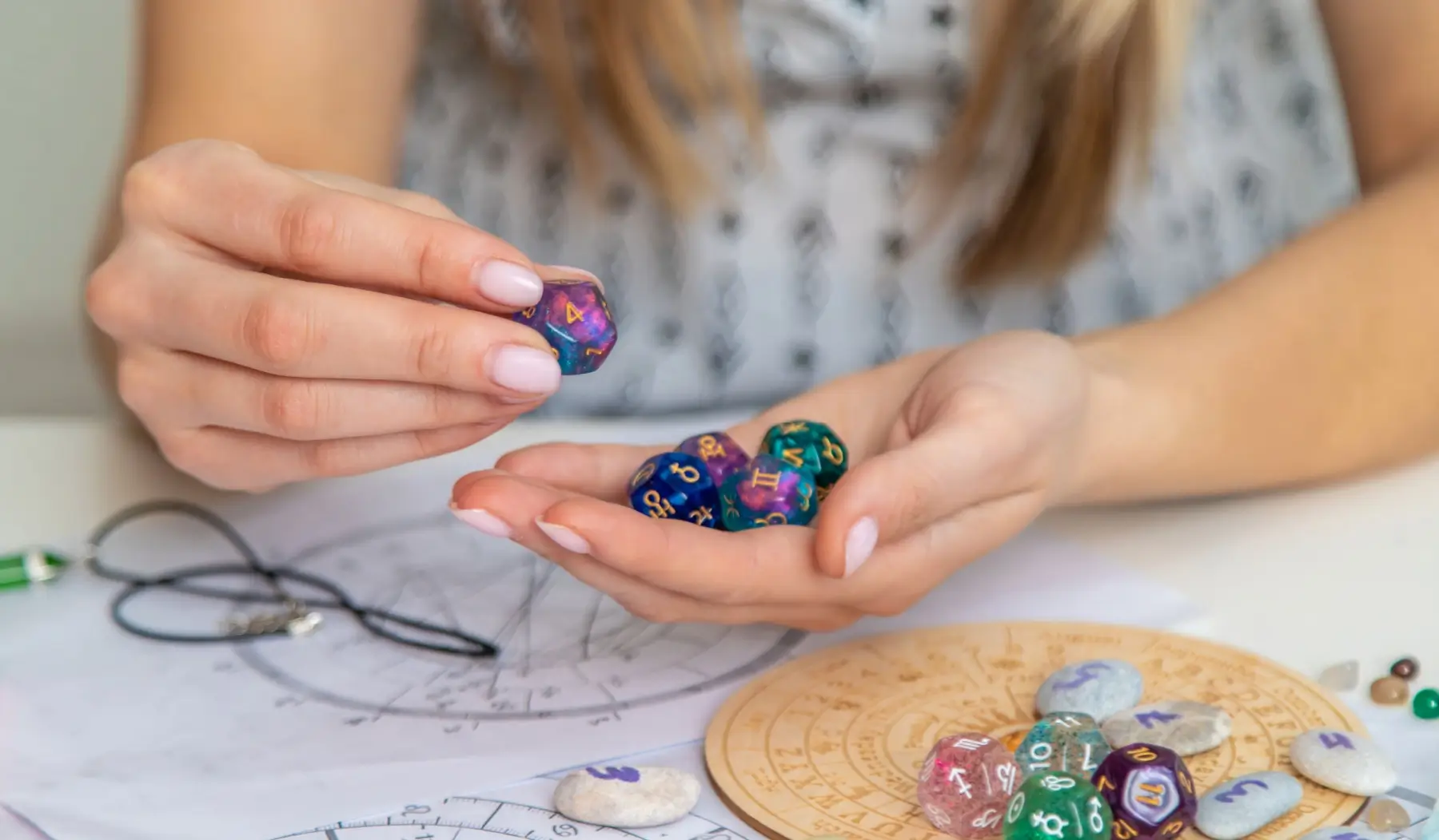 Žena drží astrologické kostky nad horoskopickým kolem na stole