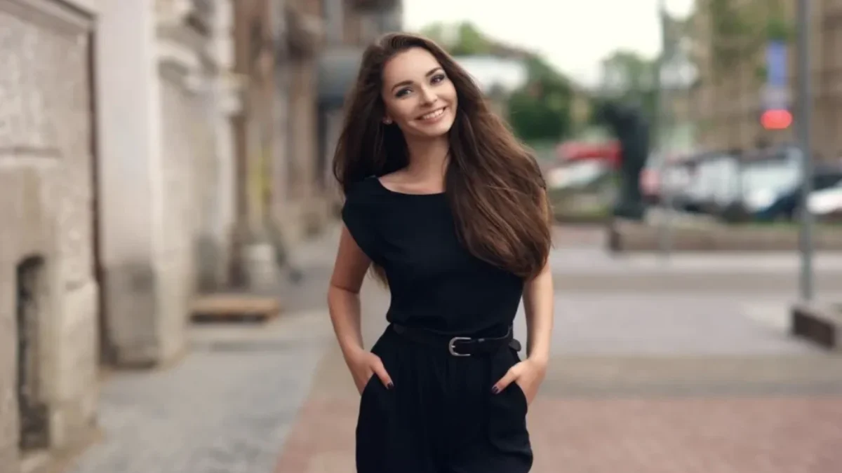 Mladá žena v černém oblečení se usmívá při procházce ulicí