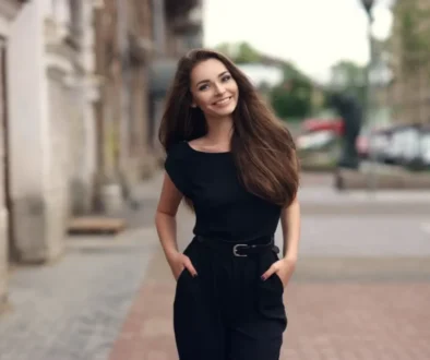 Mladá žena v černém oblečení se usmívá při procházce ulicí