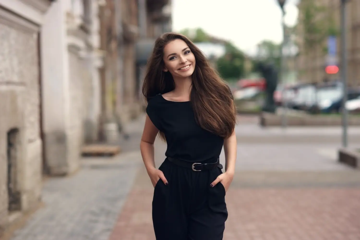 Mladá žena v černém oblečení se usmívá při procházce ulicí