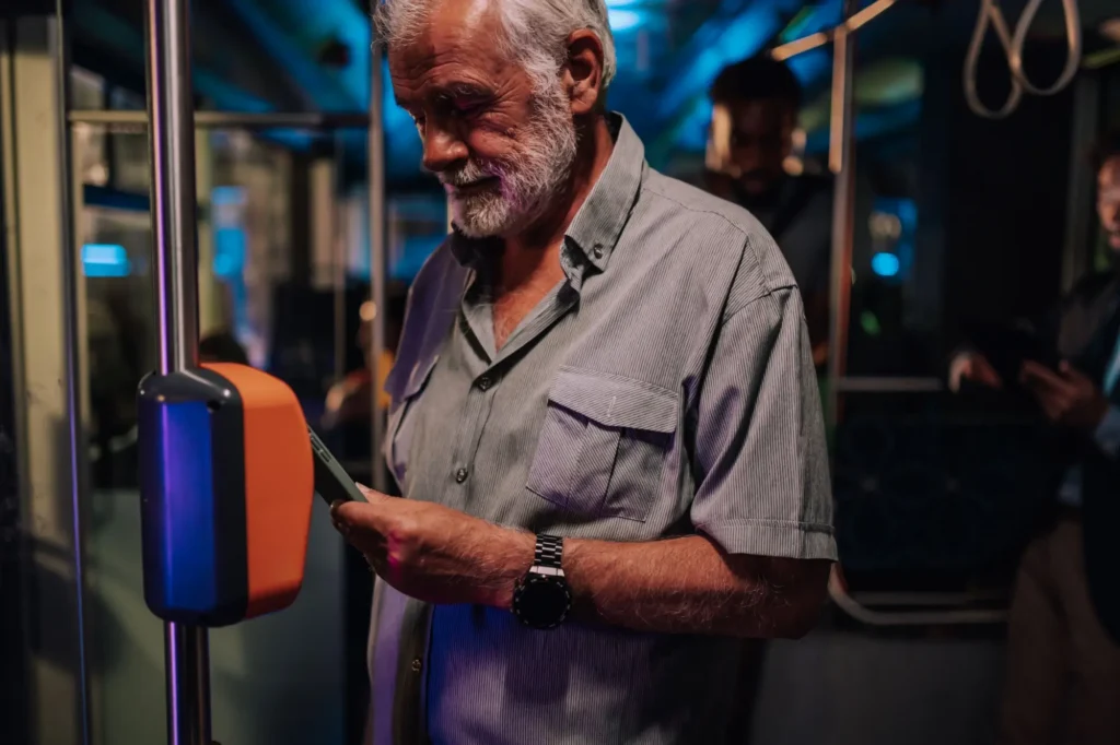 Starší muž ve večerní tramvaji přikládá telefon k validačnímu zařízení.