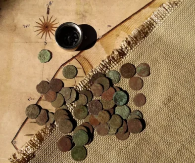 Evropské mince ze 17. století na stole s mapou a kompasem